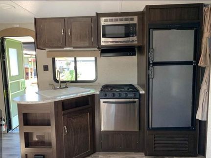 RV kitchen: dark wood cabinets, stainless steel appliances, window, sink, and counter space.