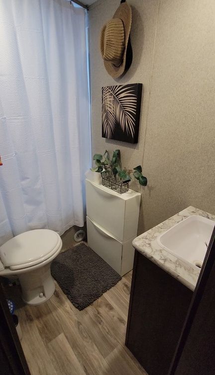 Small RV bathroom with toilet, sink, storage, artwork, and a hat hanging on the wall.