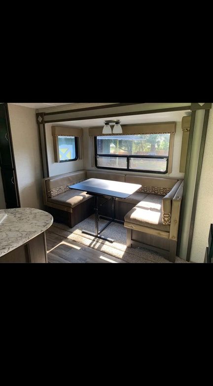 U-shaped booth seating with table in RV. Beige and brown upholstery, large window, light fixture above.