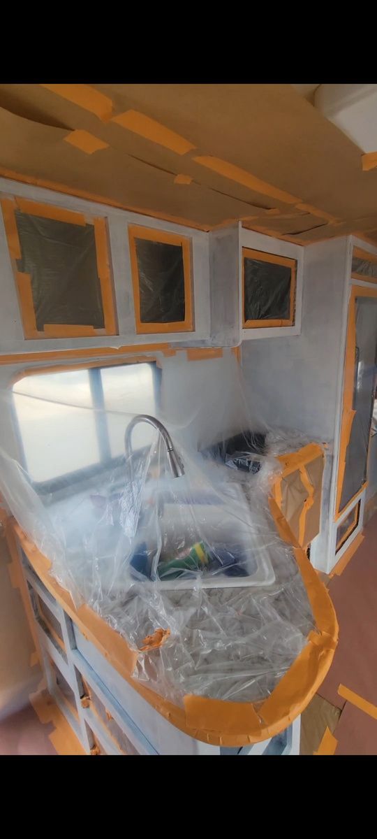 Interior of an RV during renovation, showing a sink, cabinetry, and plastic covering.