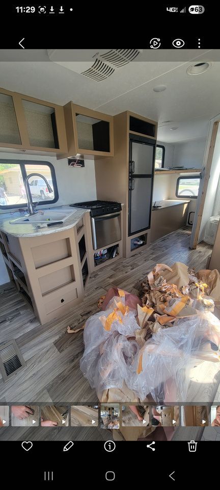 Interior of a partially-constructed RV kitchen with cabinets, appliances, and debris on the floor.
