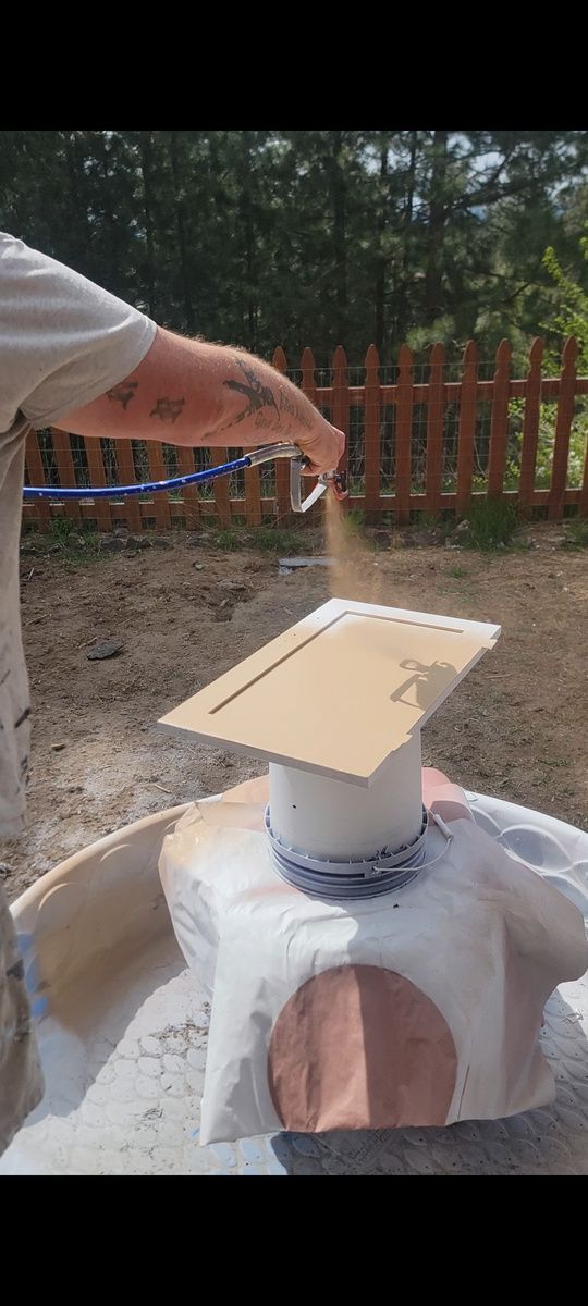 Person spraying paint on a wooden board supported by a pedestal outside.