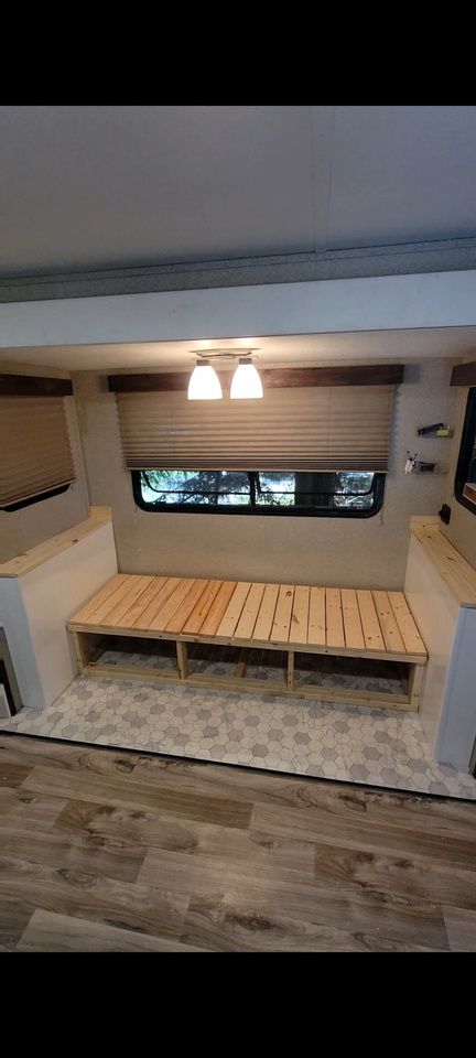 Interior of a camper with a wooden bench, window with shade, overhead lights, and patterned floor.