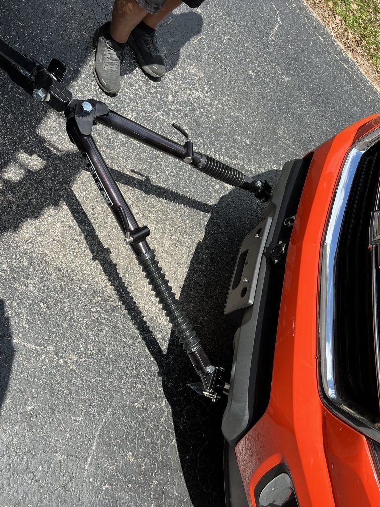 A person is standing next to a red car with a tow bar attached to it.
