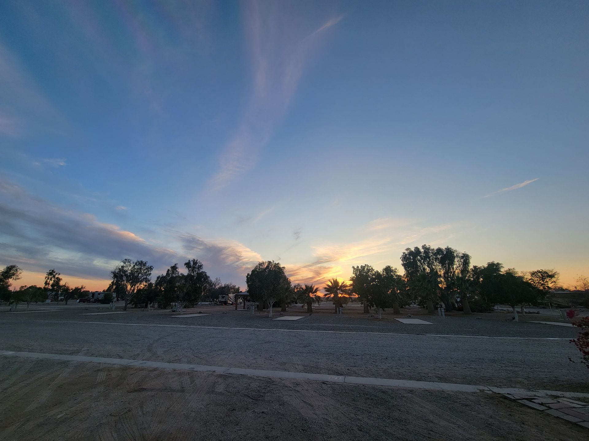 A sunset over a dirt road with trees in the background.