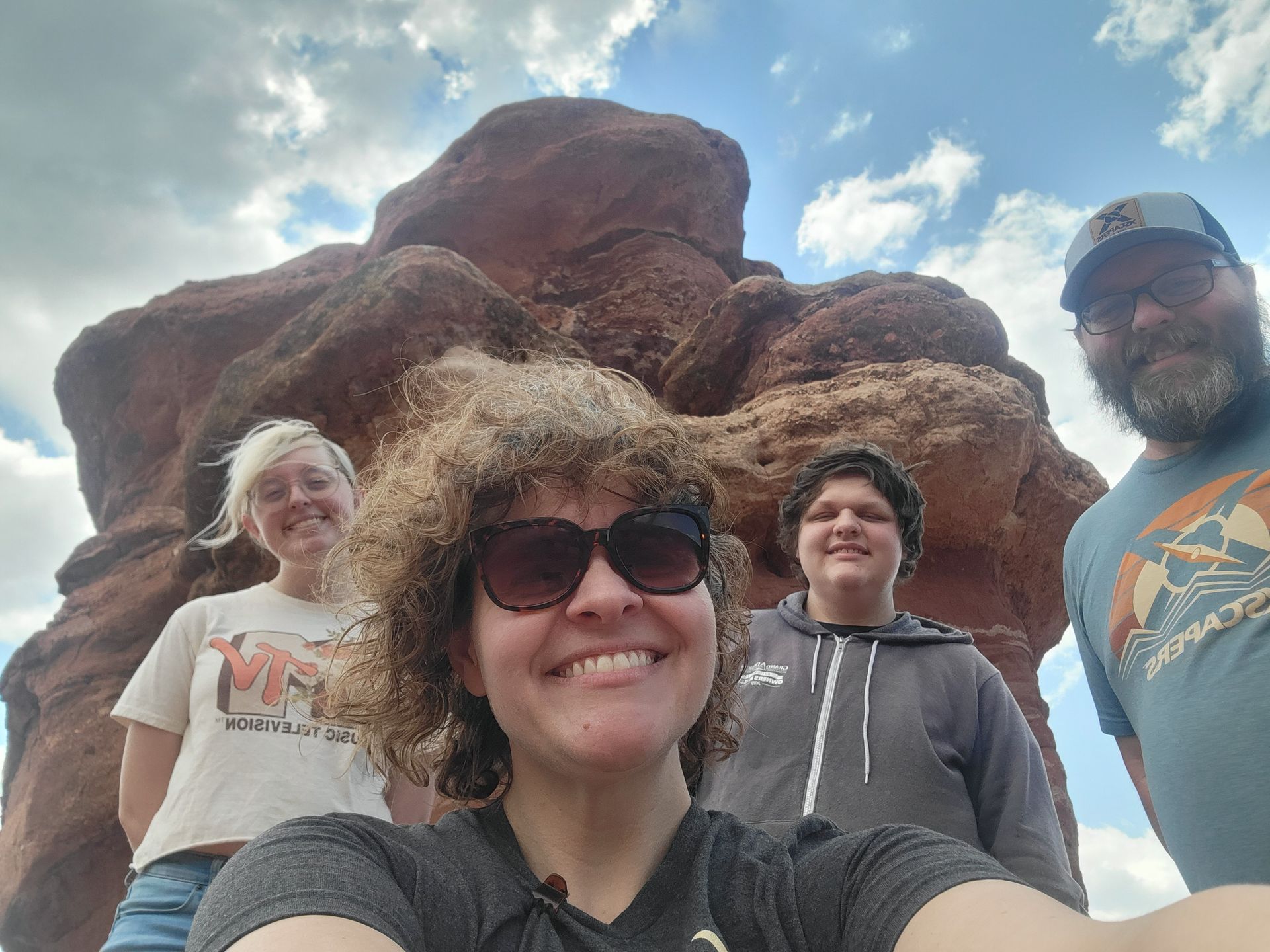 A group of people are posing for a selfie in front of a large rock formation.