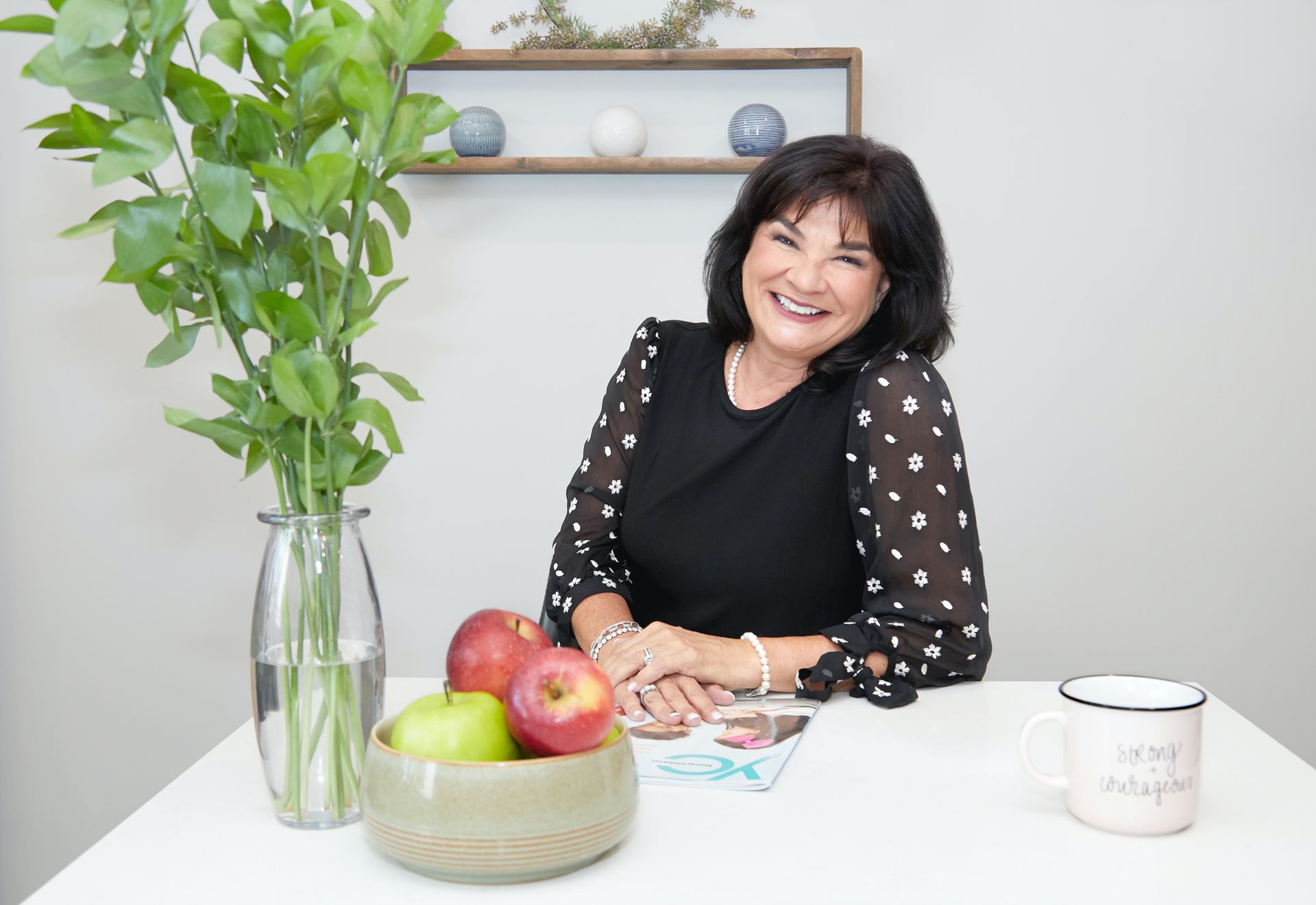 Woman with glasses smiles; silver and brown hair; stickers on wooden background.
