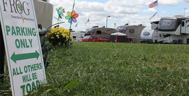 A parking only sign is in the grass in front of a rv park.