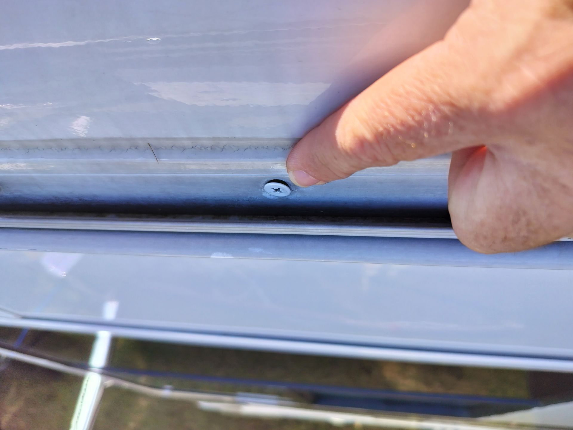 A person is pointing at a screw on the side of a car.