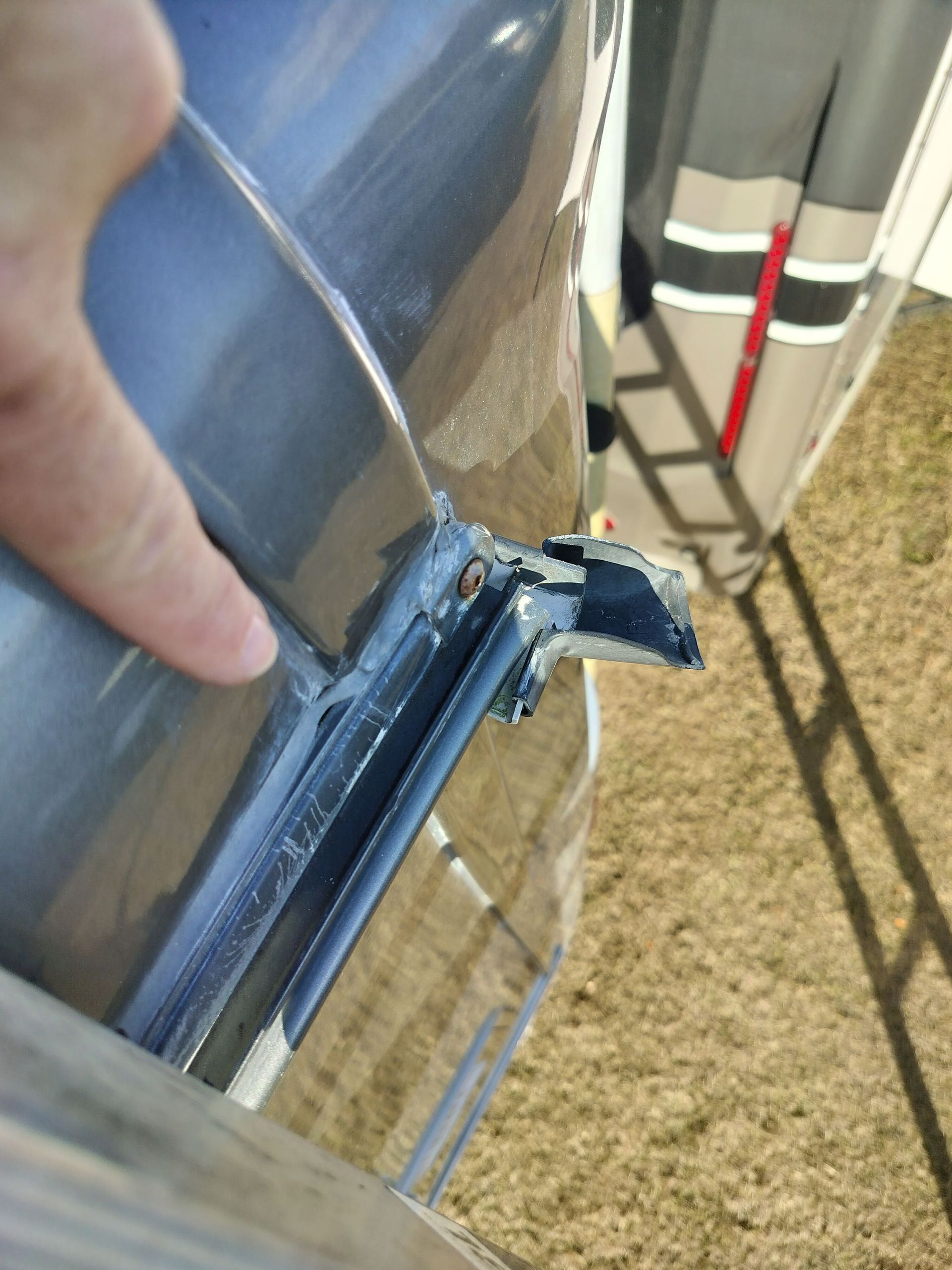 A close-up view of a damaged roof trim component on an RV or camper, with a finger pointing to the broken plastic joint.
