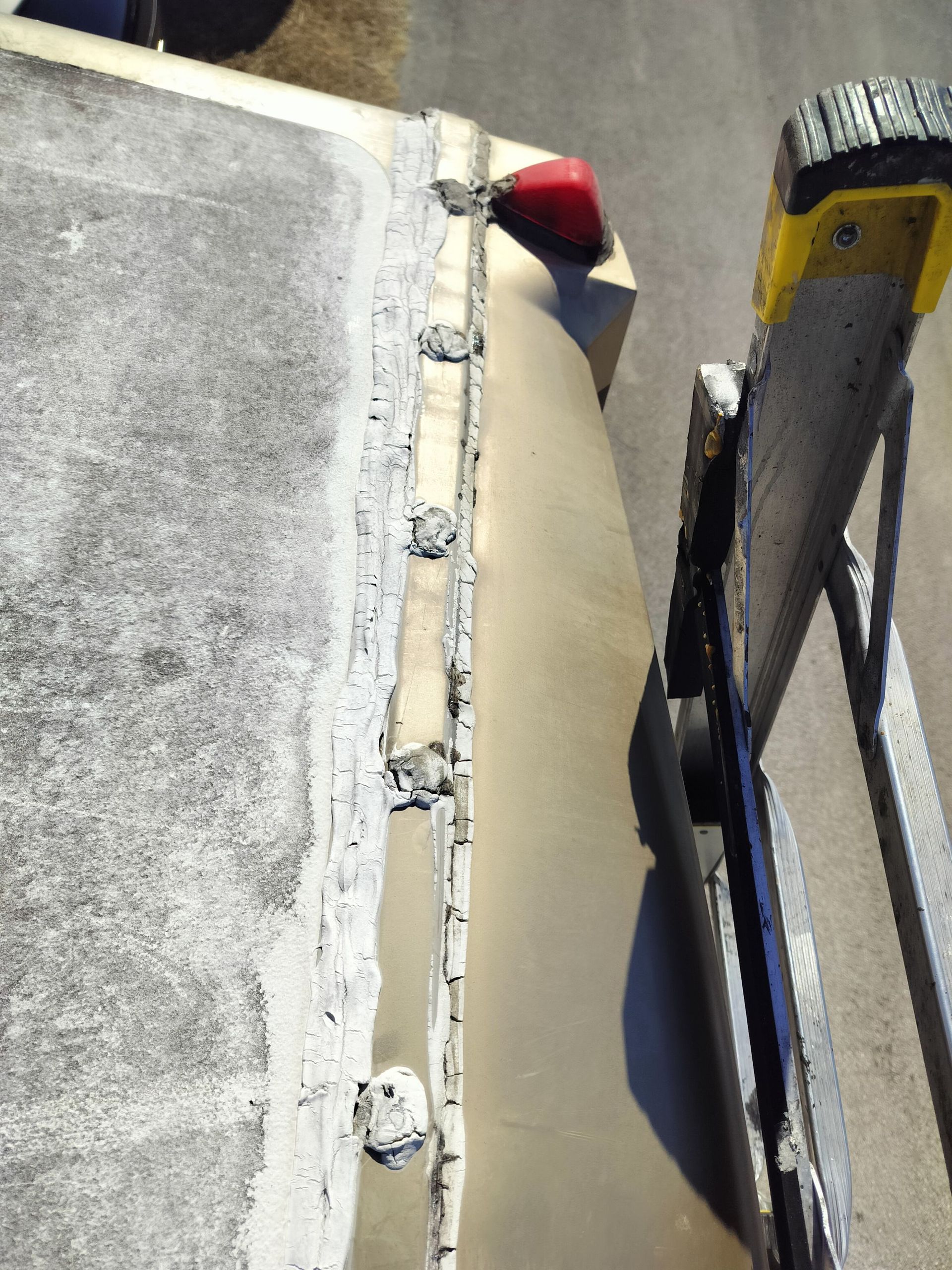 A view of an RV roof edge with weathered sealant and a ladder leaning against the side.