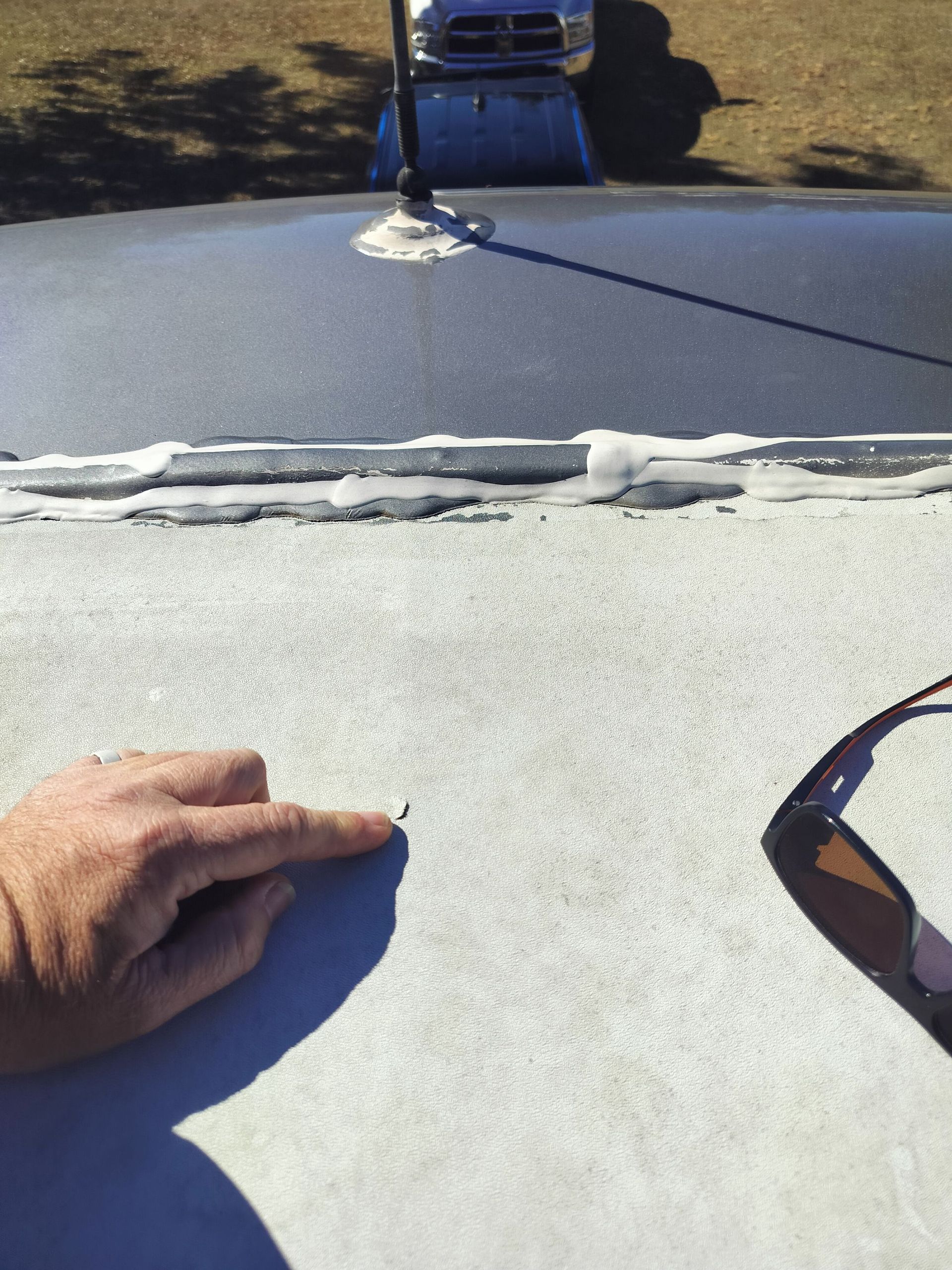 A person's finger points to a small puncture in the white rubber membrane of an RV roof near a seam and antenna.