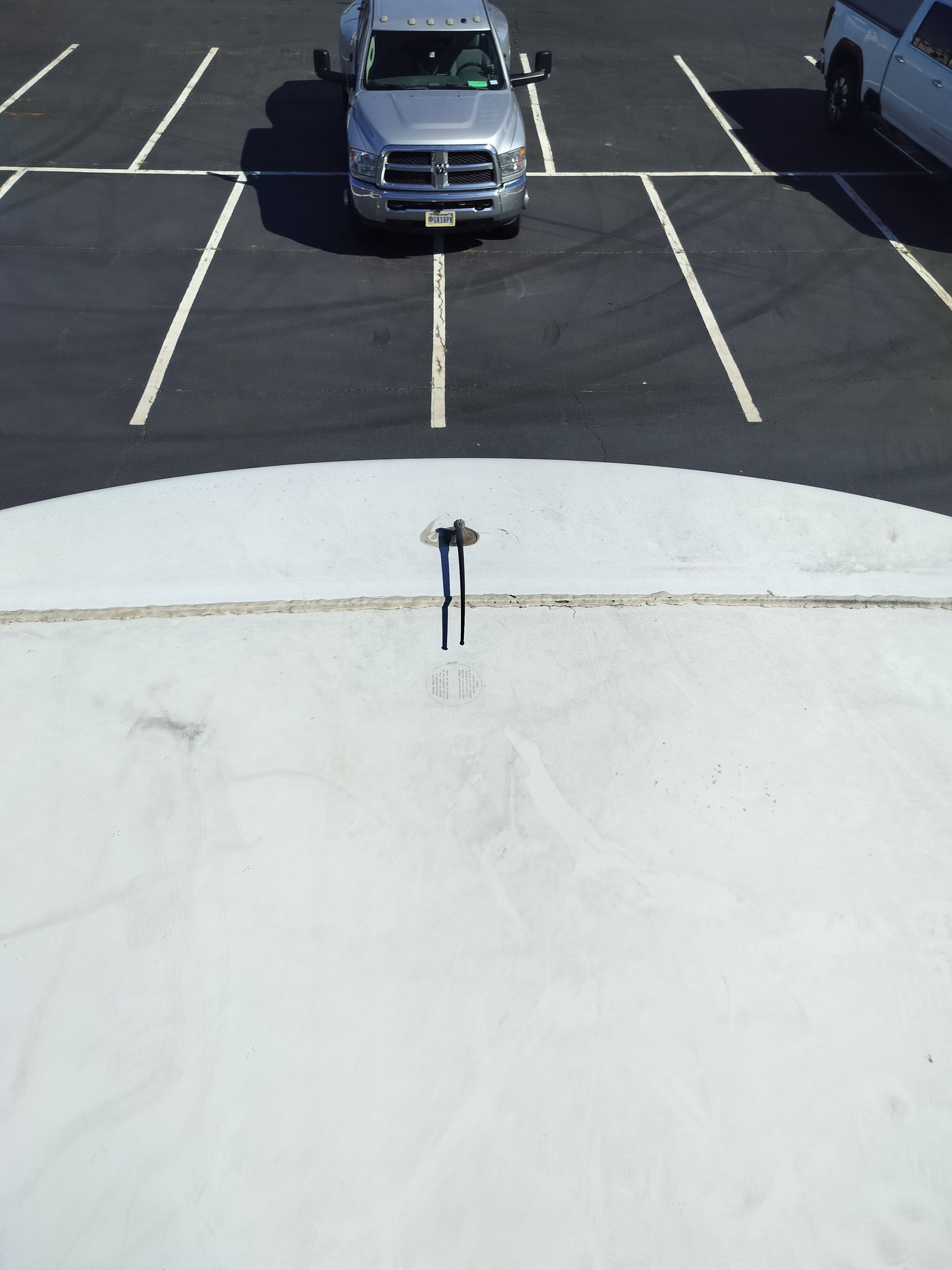 An antenna on a white rv roof surface, overlooking a parking lot with two pickup trucks.