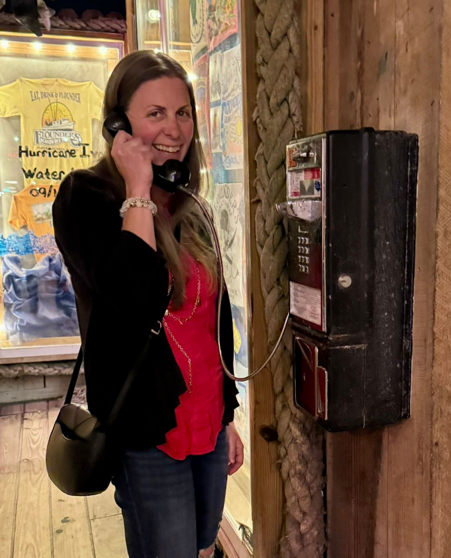 Women on a pay phone smiling with a purse, red shirt and black jacket