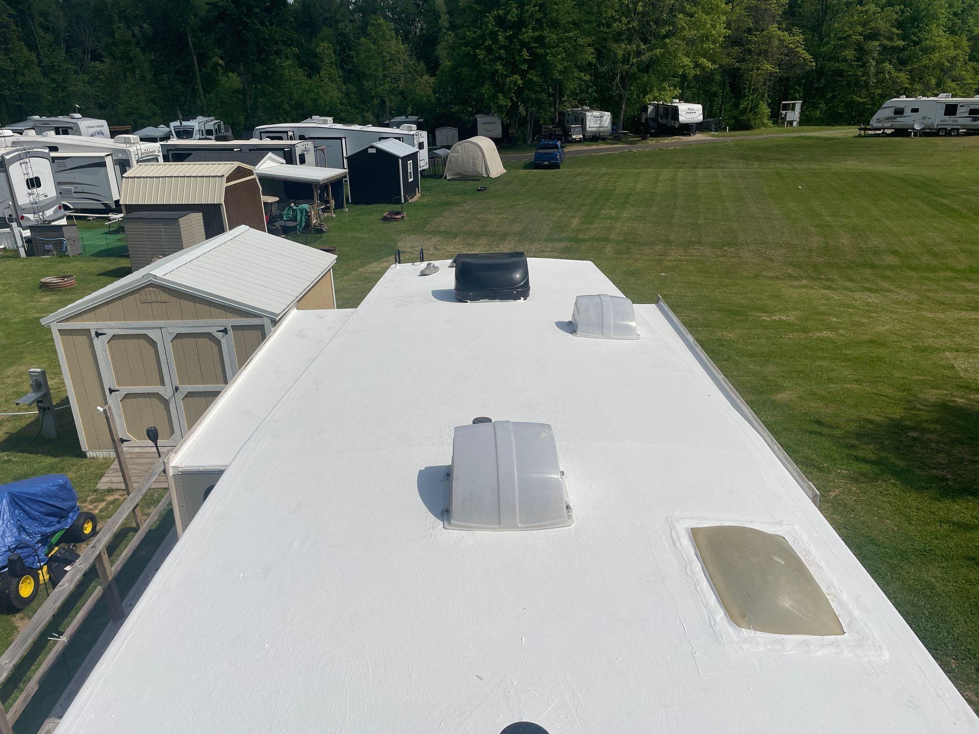 White RV trailer roof with vents and skylights in a grassy campground surrounded by other campers.
