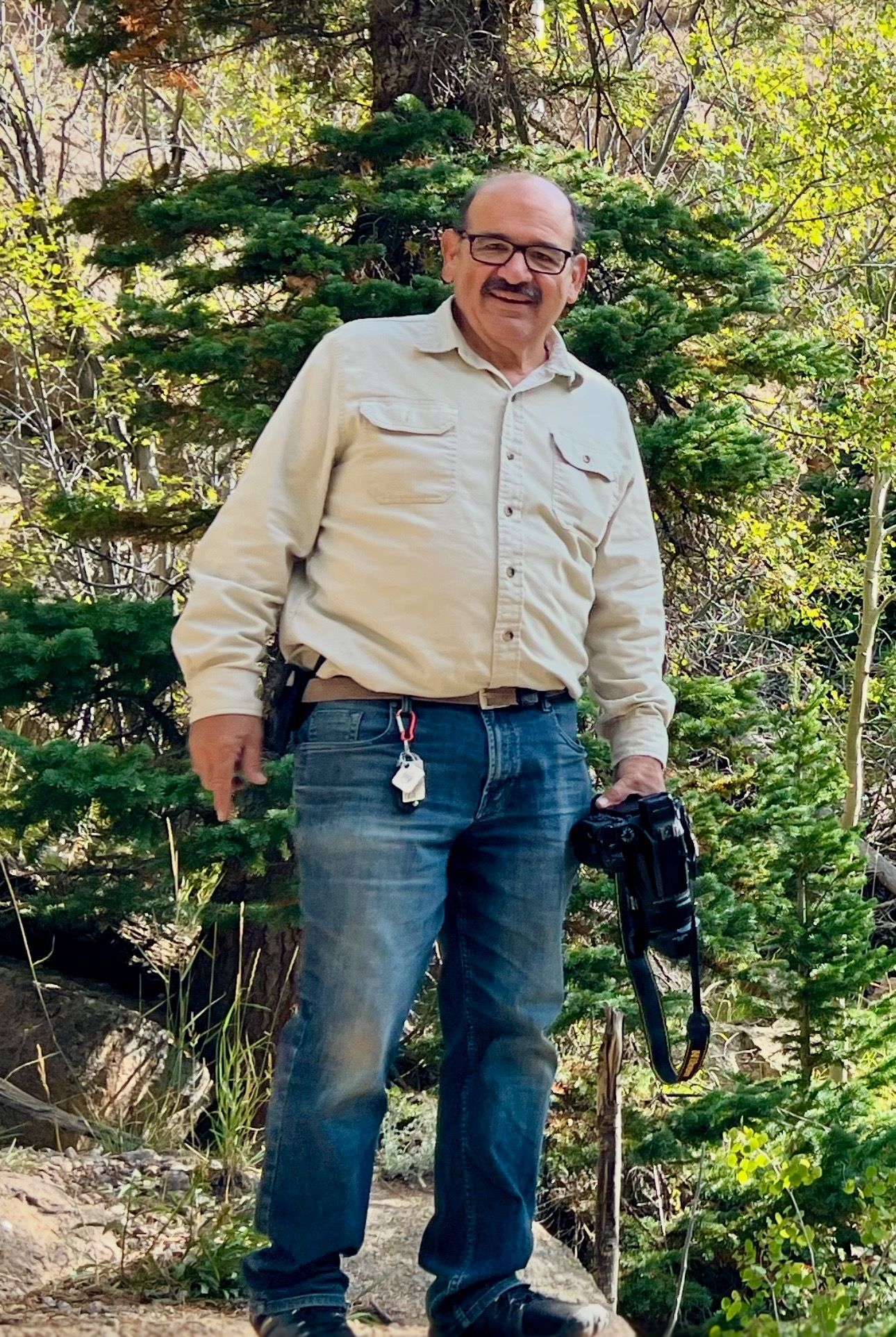 A man is standing in the woods holding a camera.