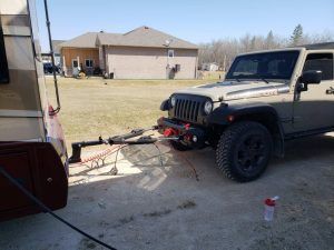 A jeep is towing a trailer in a parking lot.