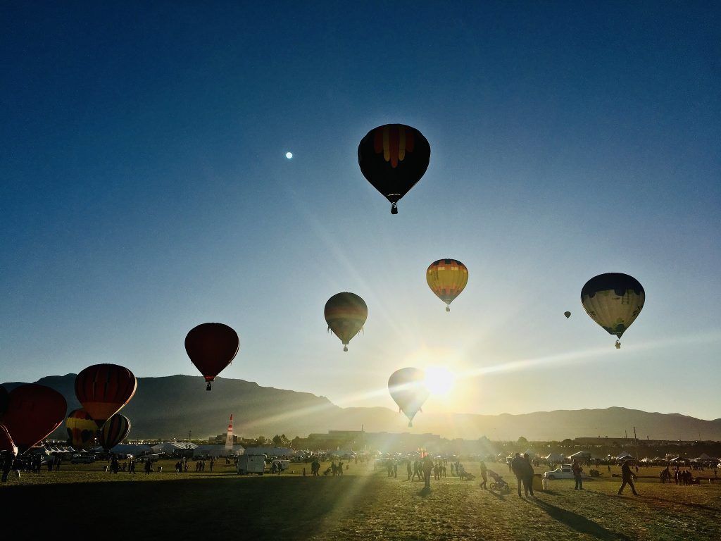 Hot air balloons in the early morning with the sun peaking out behind a balloon
