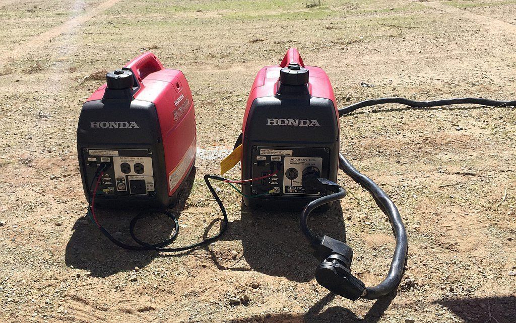 Two generators are sitting next to each other on the ground.