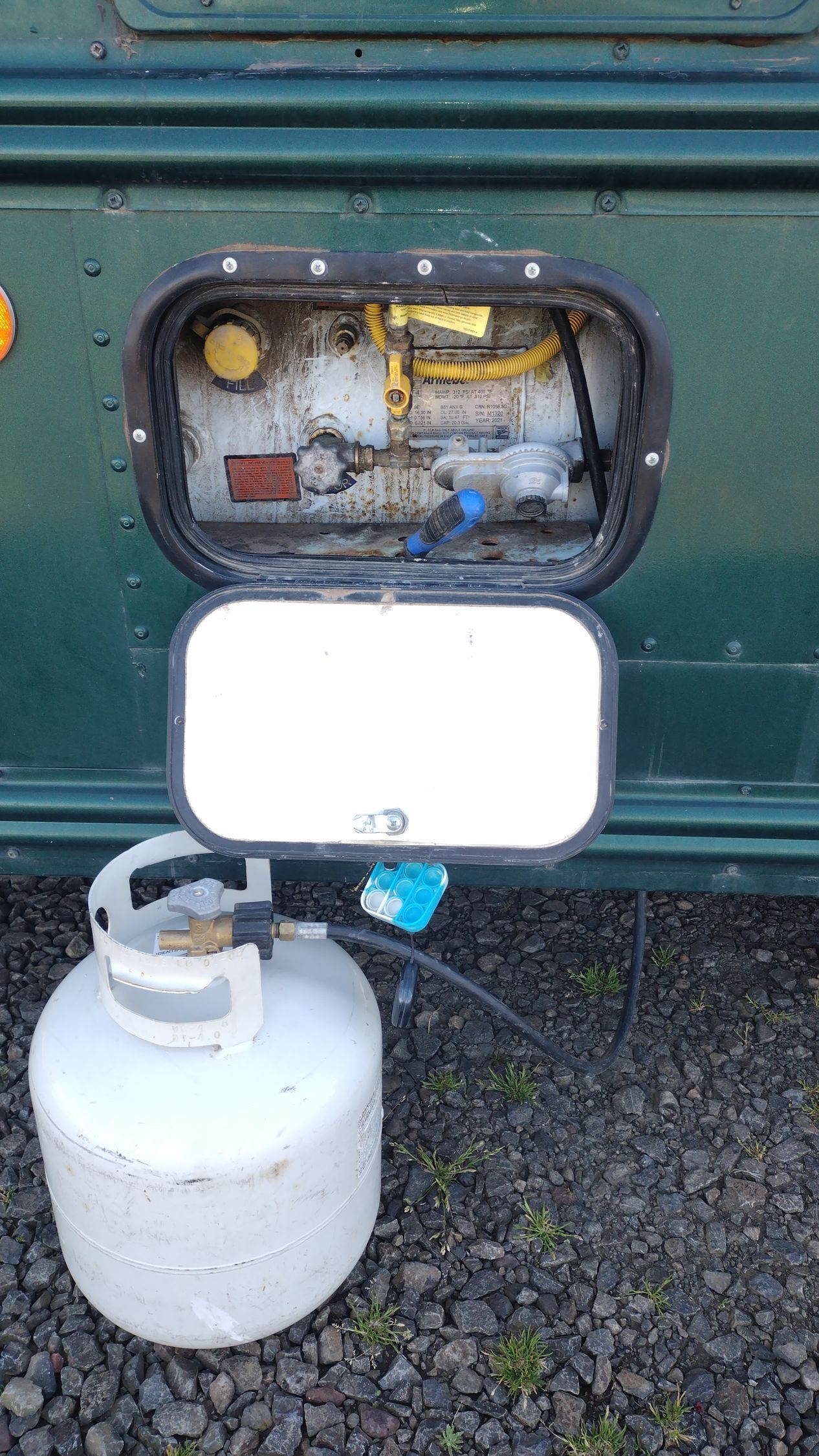 A propane tank is attached to the side of a green vehicle.