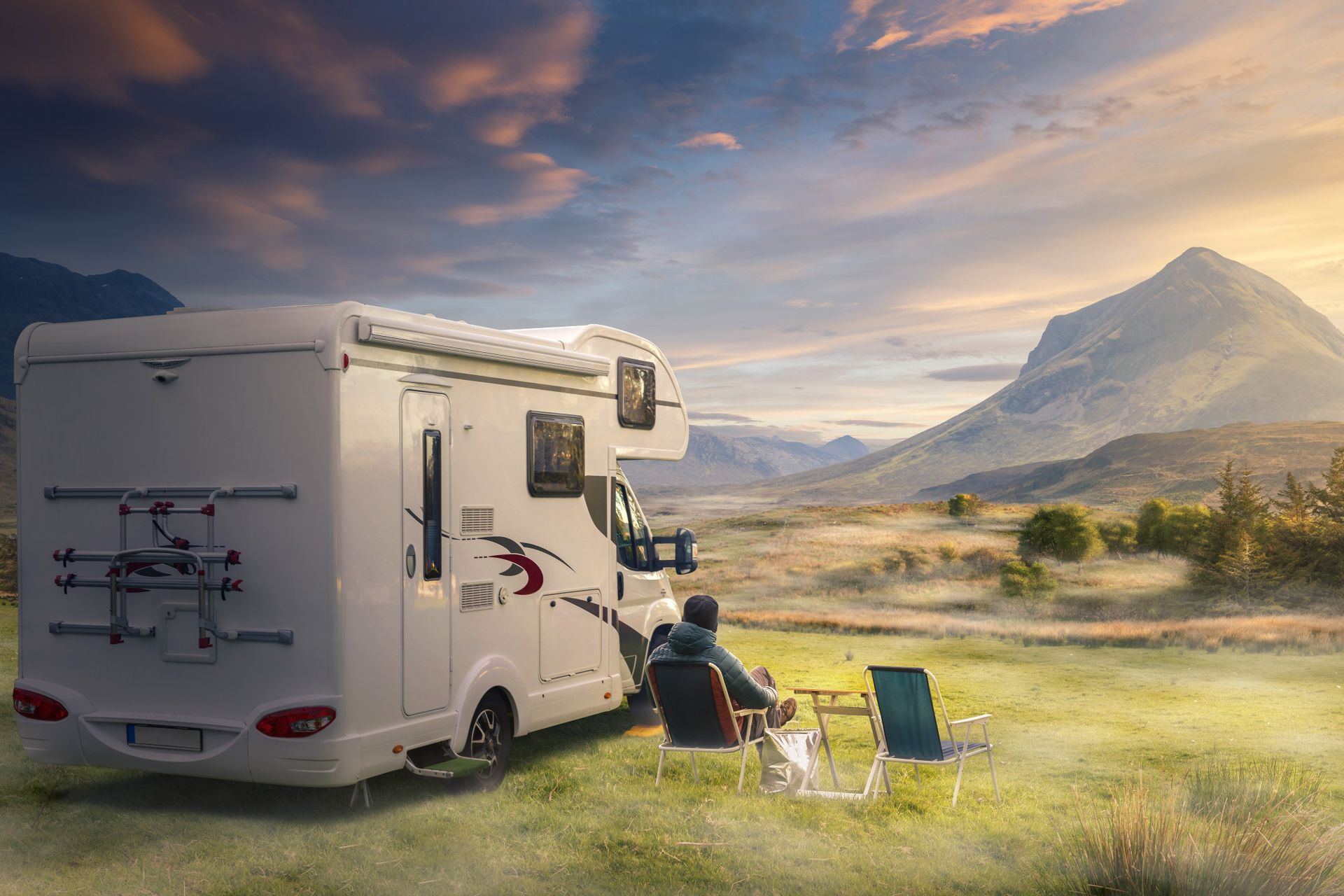 A man is sitting in a chair next to a rv in a field.