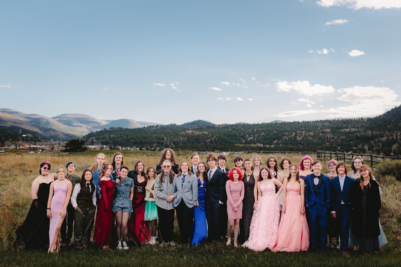 A large group of people are posing for a picture in a field with mountains in the background.