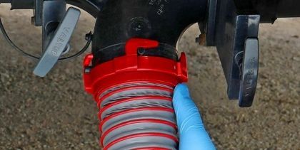 Close-up of a red and gray flexible hose attached to machinery, with a blue gloved hand holding it.