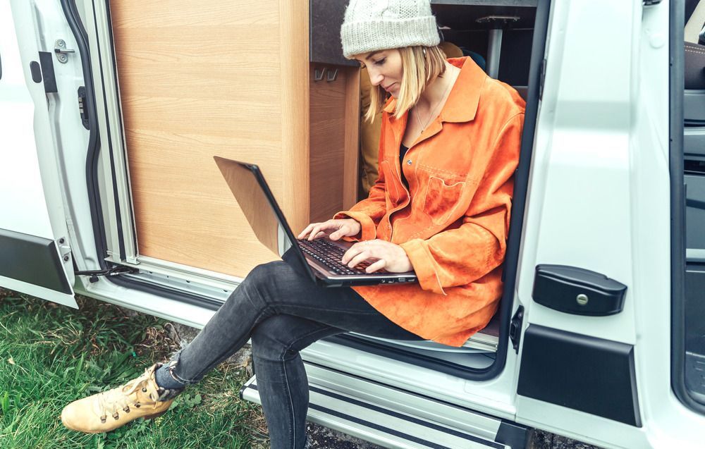 A woman is sitting in the back of a van using a laptop computer.