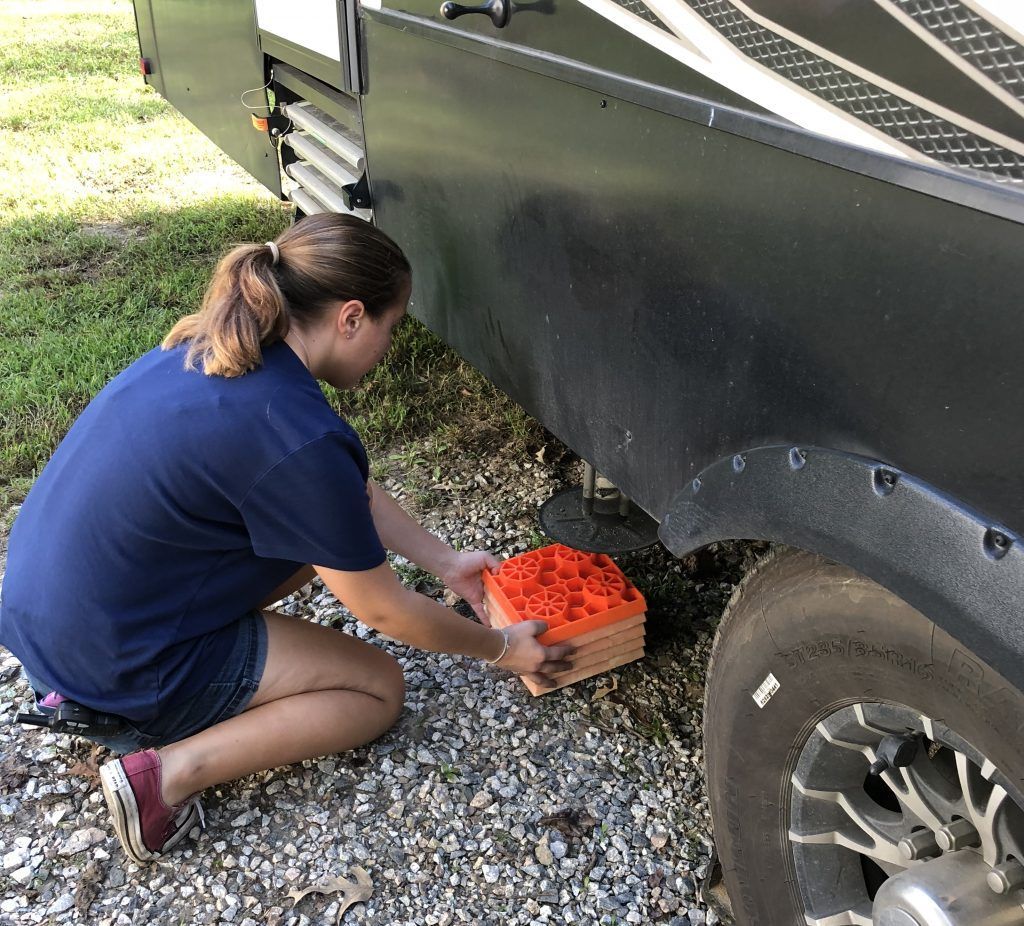 A woman in a blue shirt is kneeling next to a rv