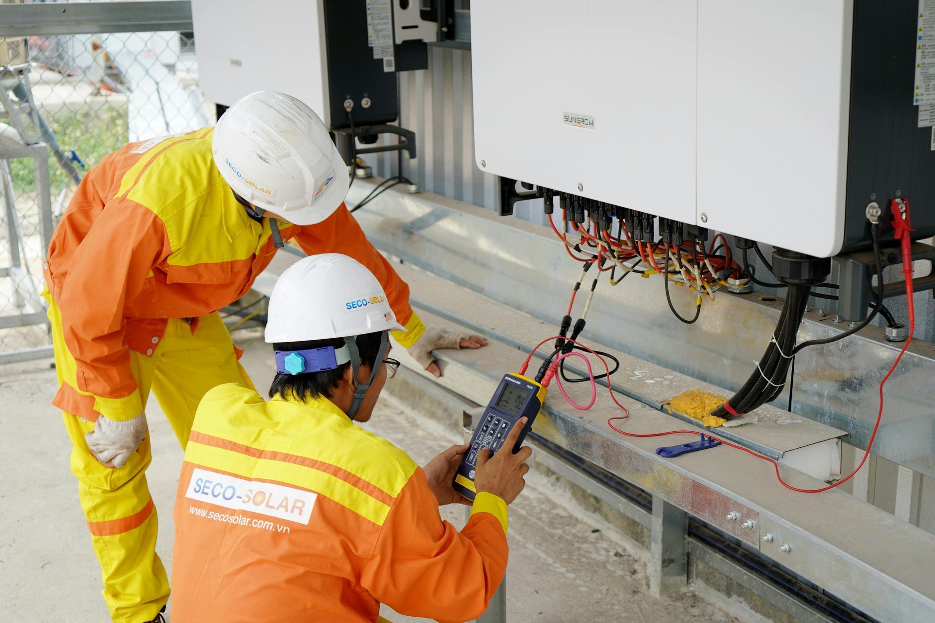 Two men in hard hats are working on a solar panel.