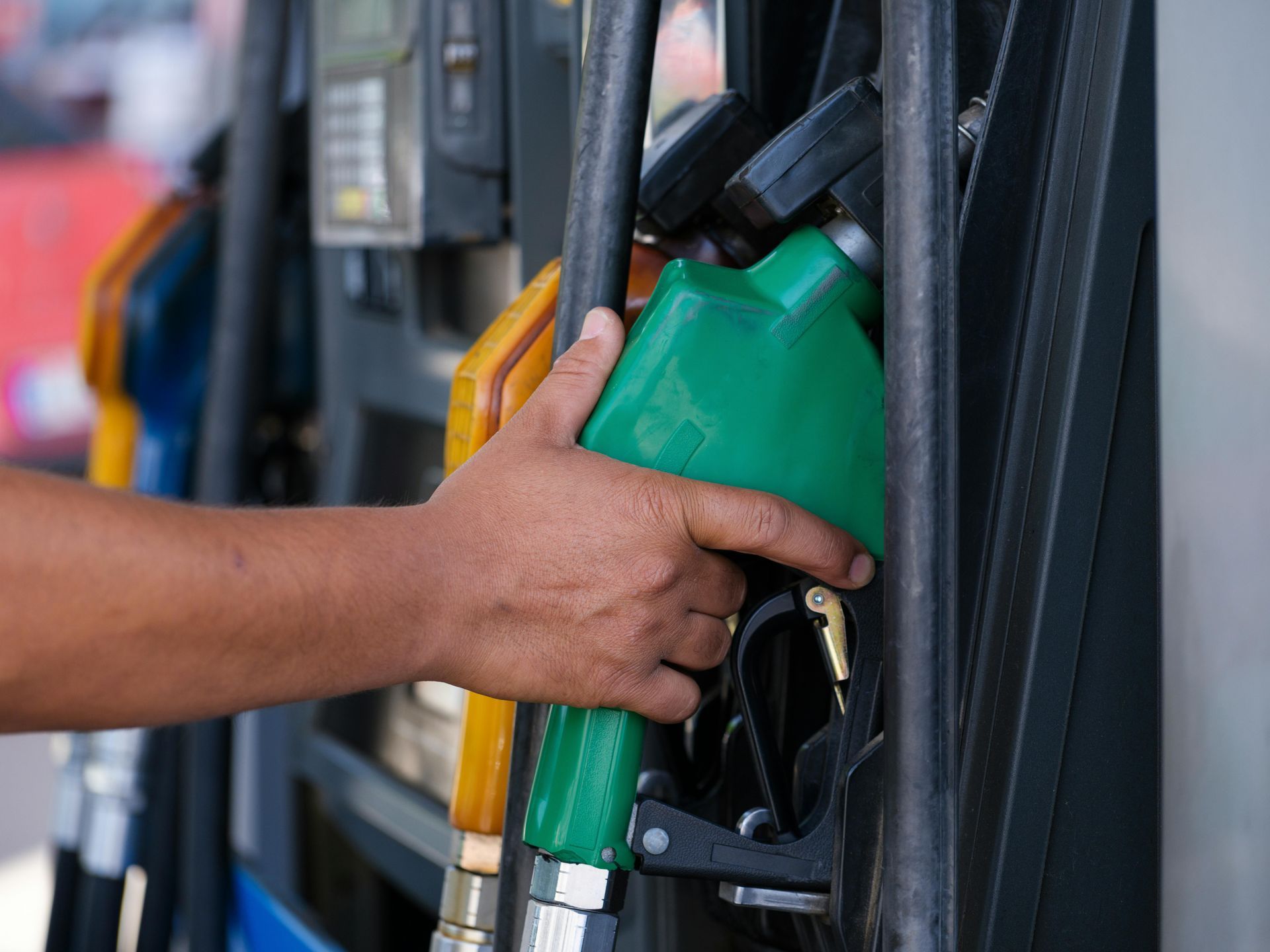 Hand refueling a vehicle with a green fuel nozzle at a gas station
