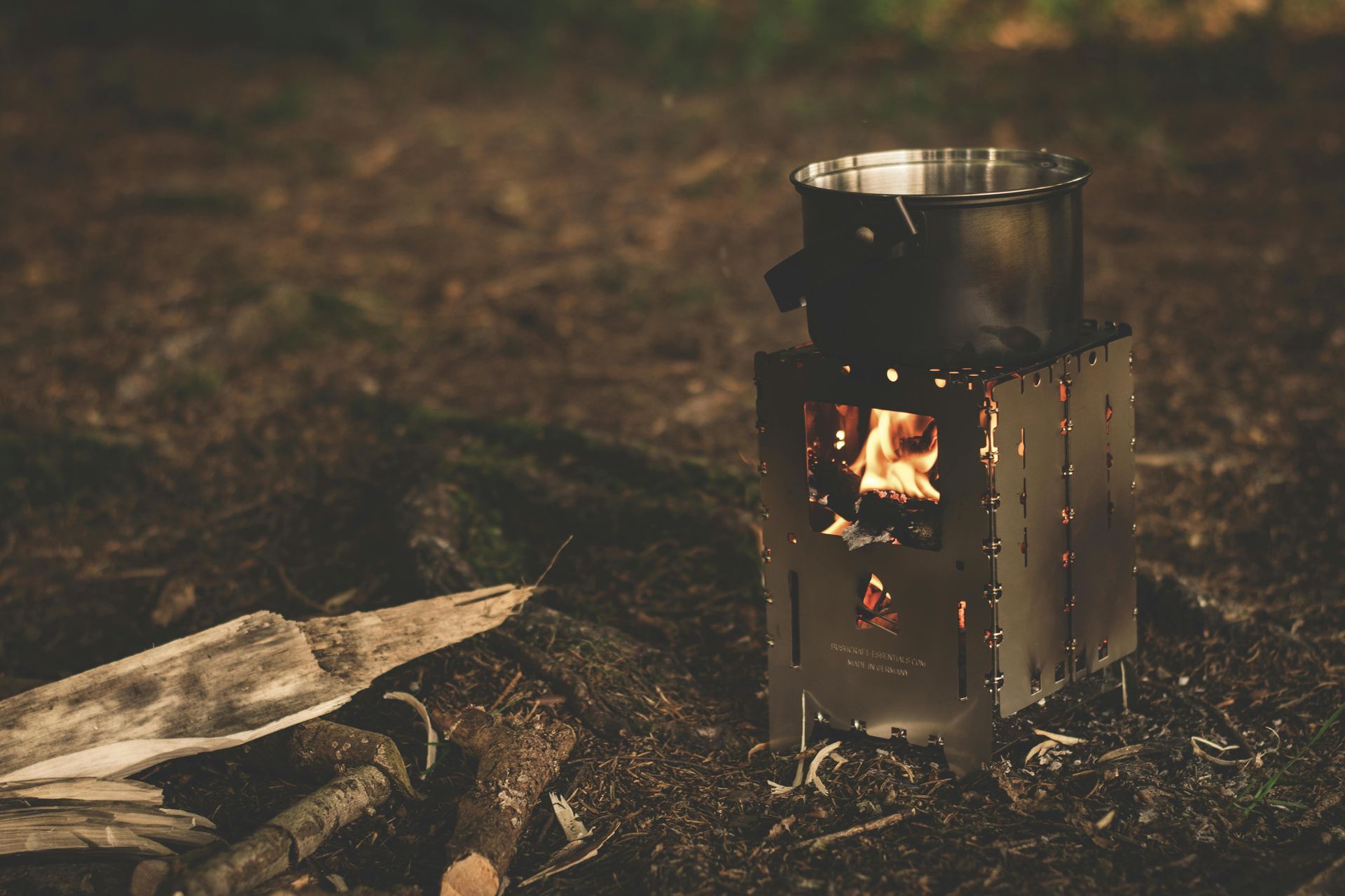 A pot is cooking on a small wood stove in the woods.