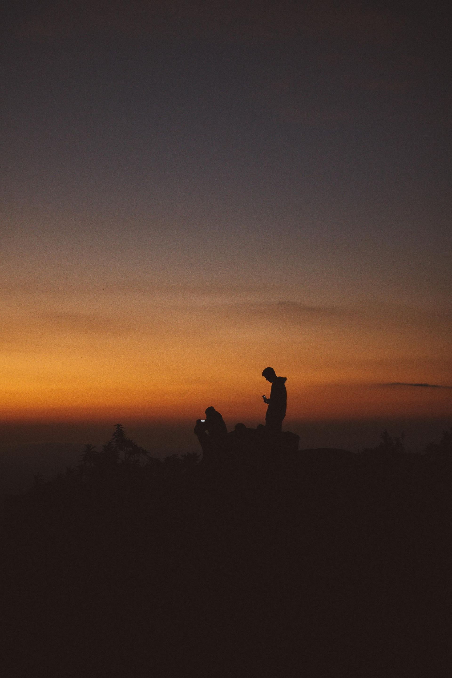 A man is standing on top of a hill at sunset.