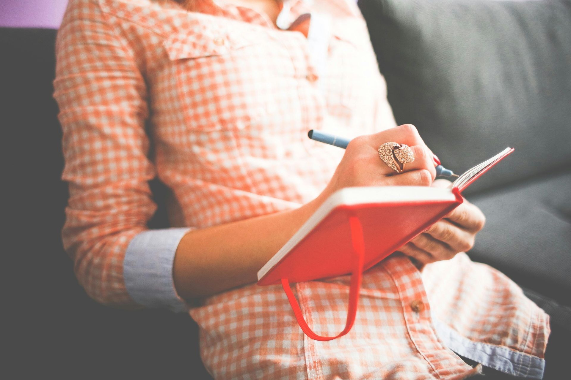 A woman is sitting on a couch writing in a notebook.