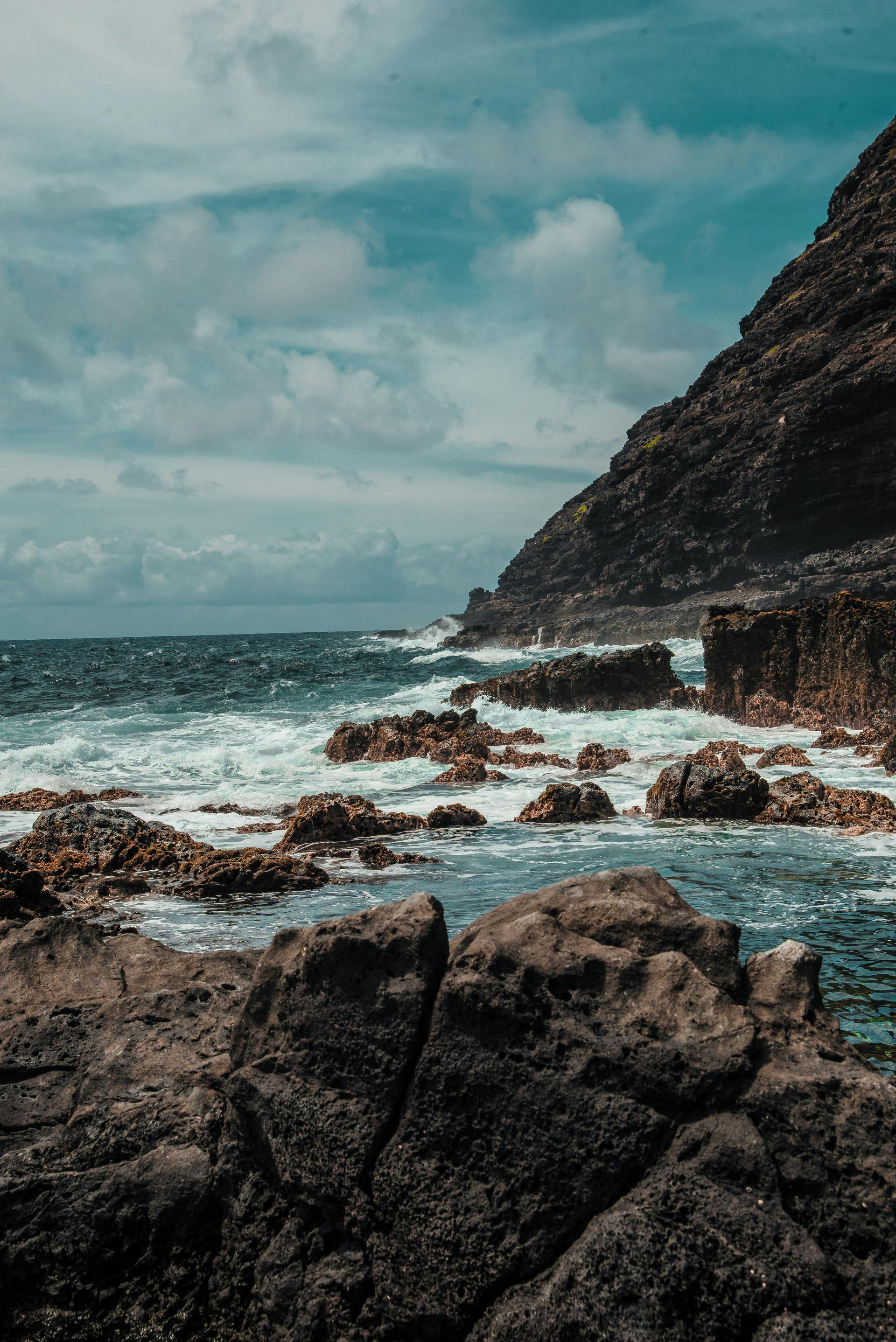 A rocky shoreline with waves crashing against the rocks on a sunny day.