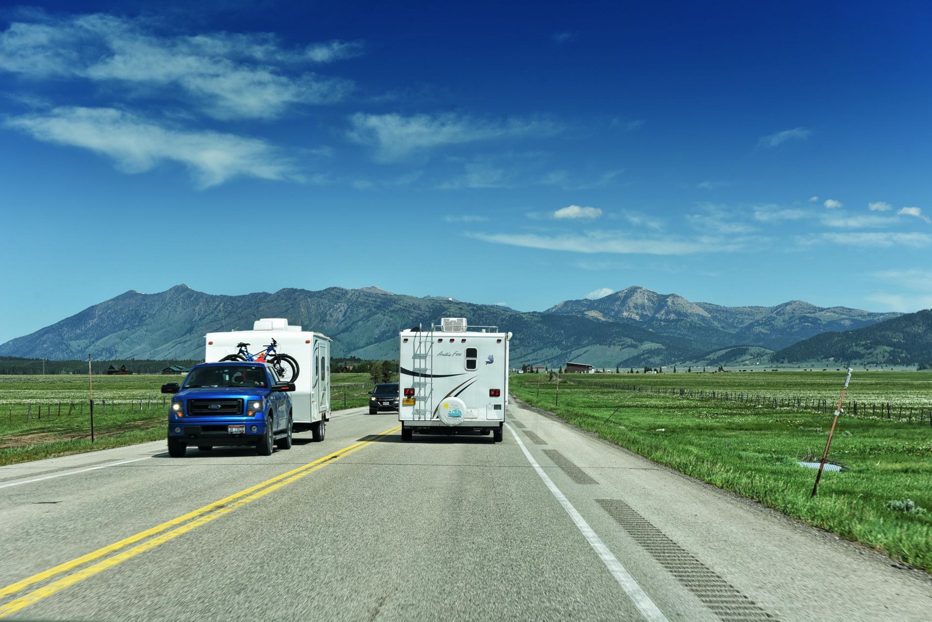 A truck is pulling a trailer down a road with mountains in the background.
