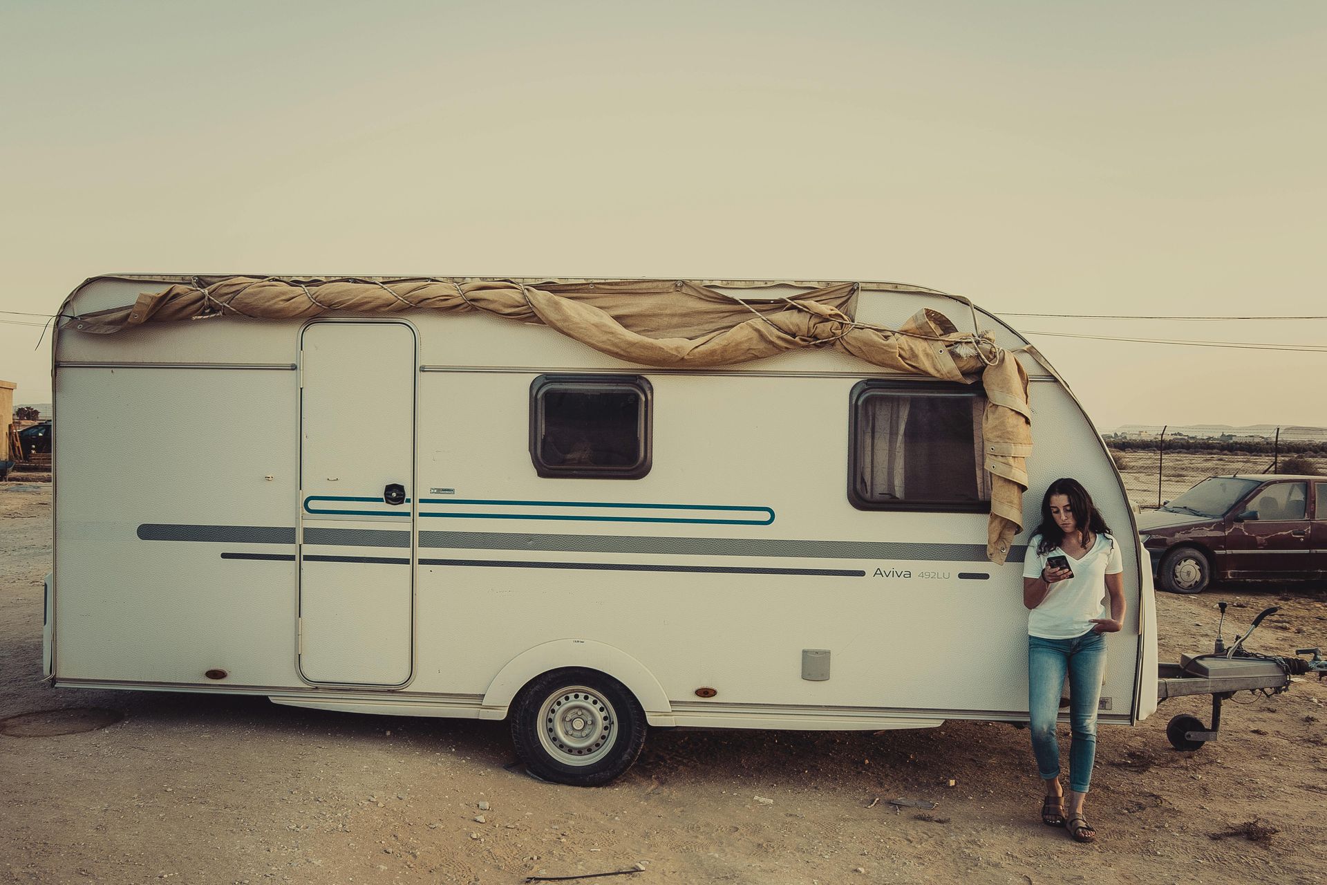 A woman is standing next to a trailer in the desert.