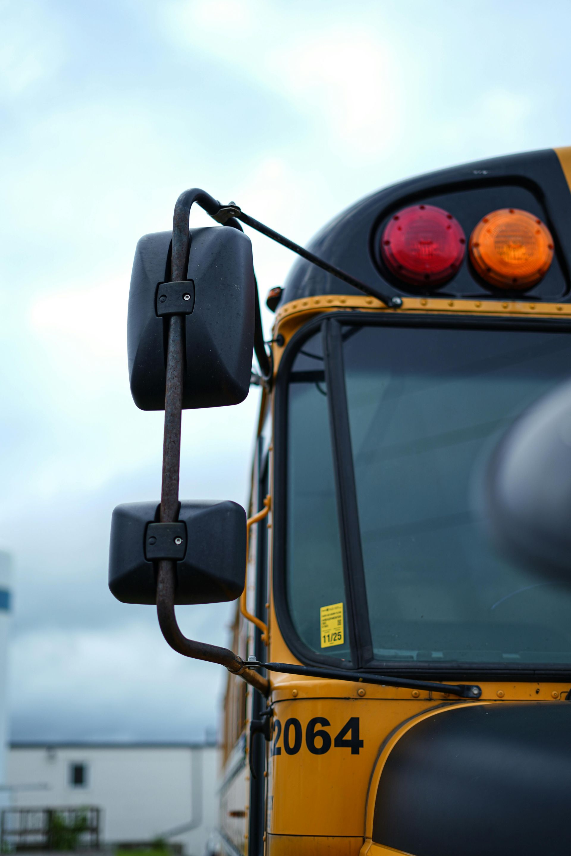 Yellow school bus with side mirrors and signal lights against a cloudy sky.