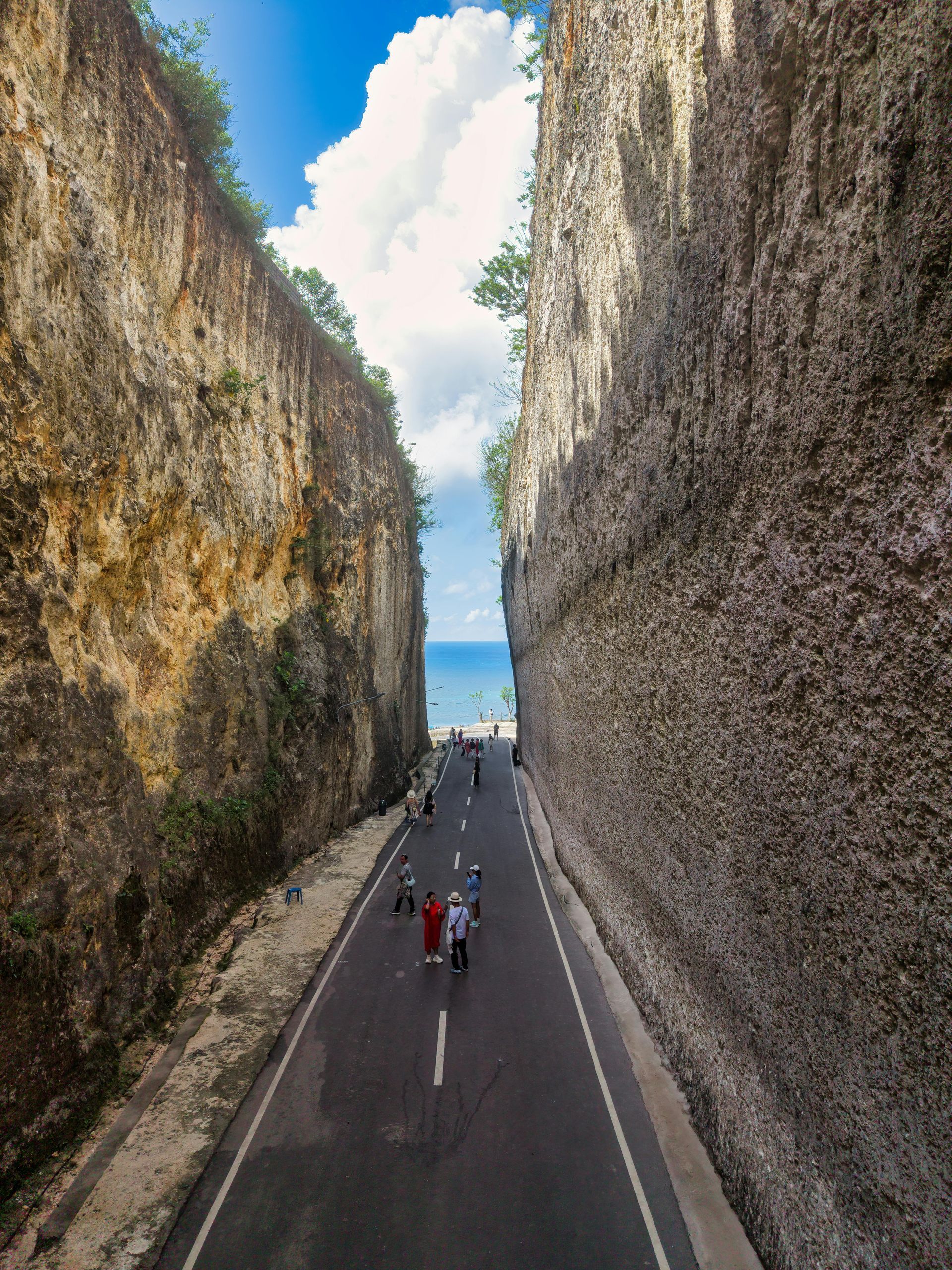 People walking between tall rocky cliffs toward the sea on a narrow road