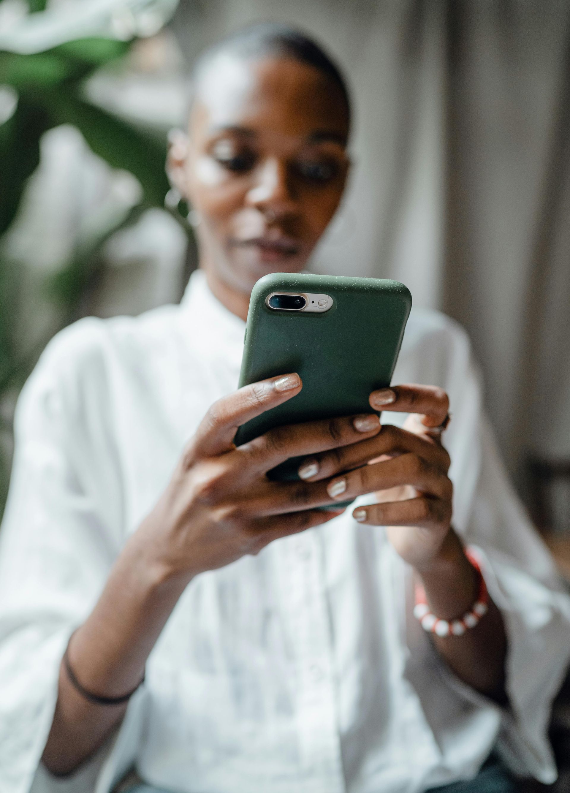 A person in a white shirt holding a dark green smartphone, focused on the screen in a brightly lit indoor space.
