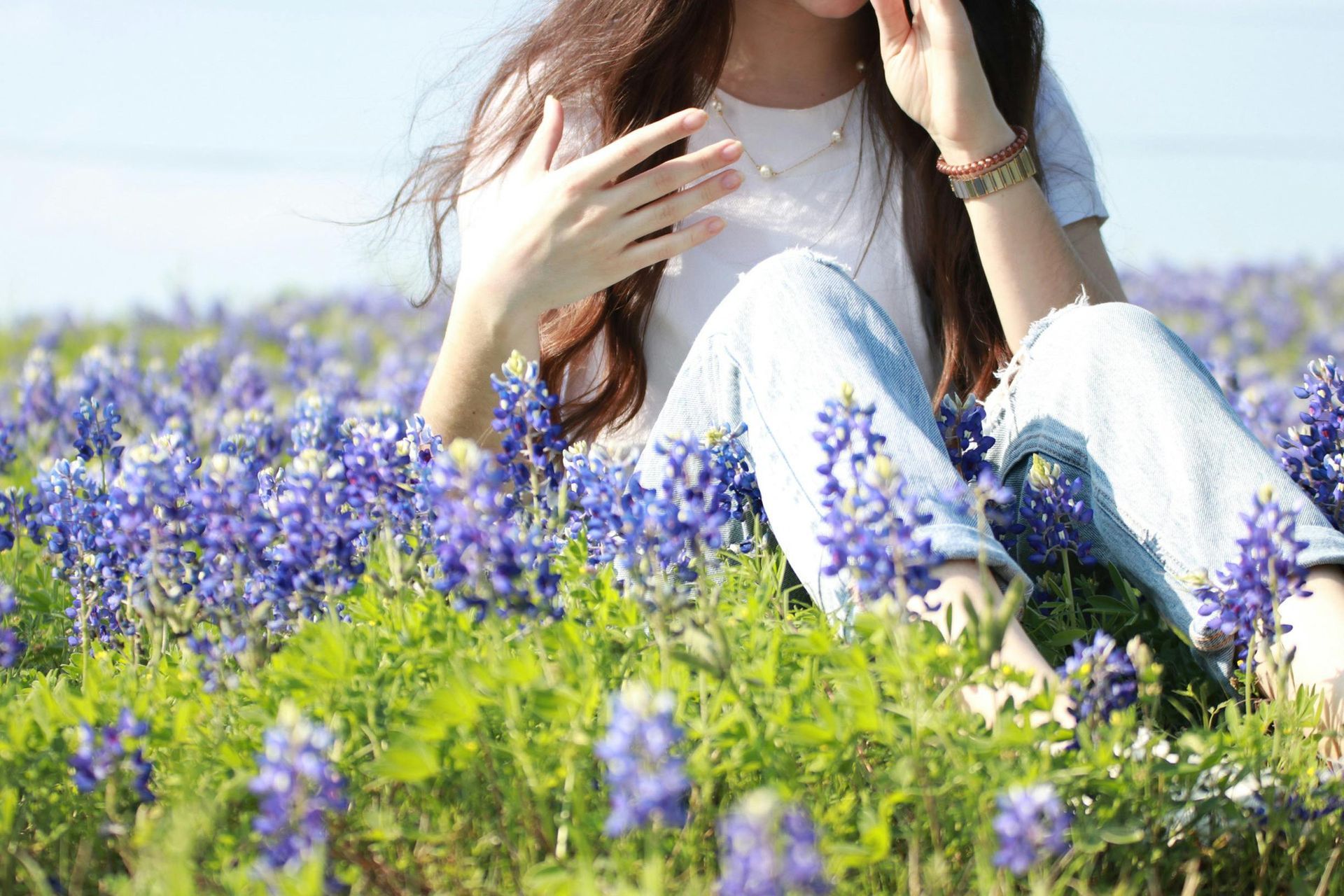 A person sitting in a field of blooming bluebonnet flowers on a sunny day.