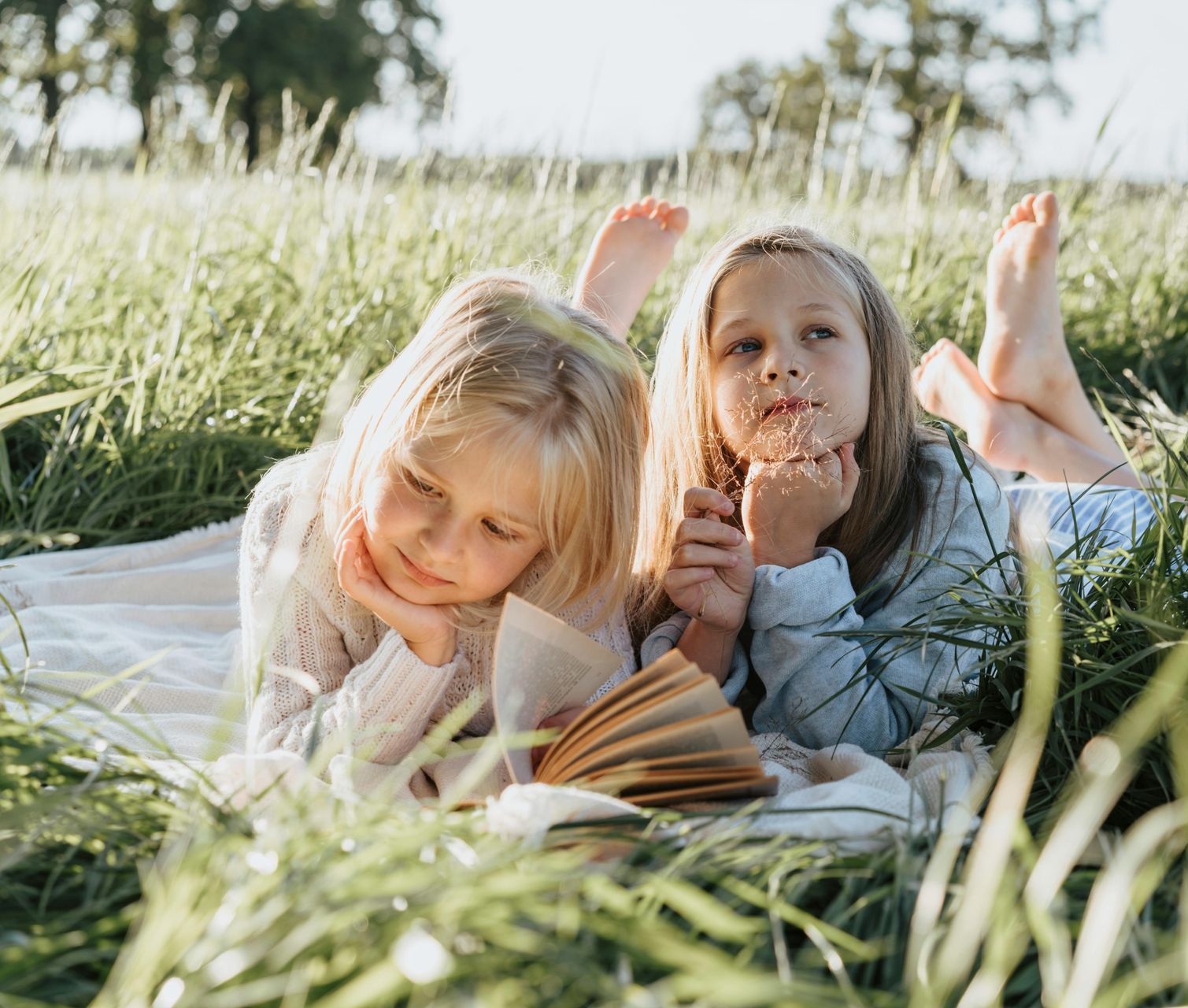 Two little girls are laying in the grass reading a book.