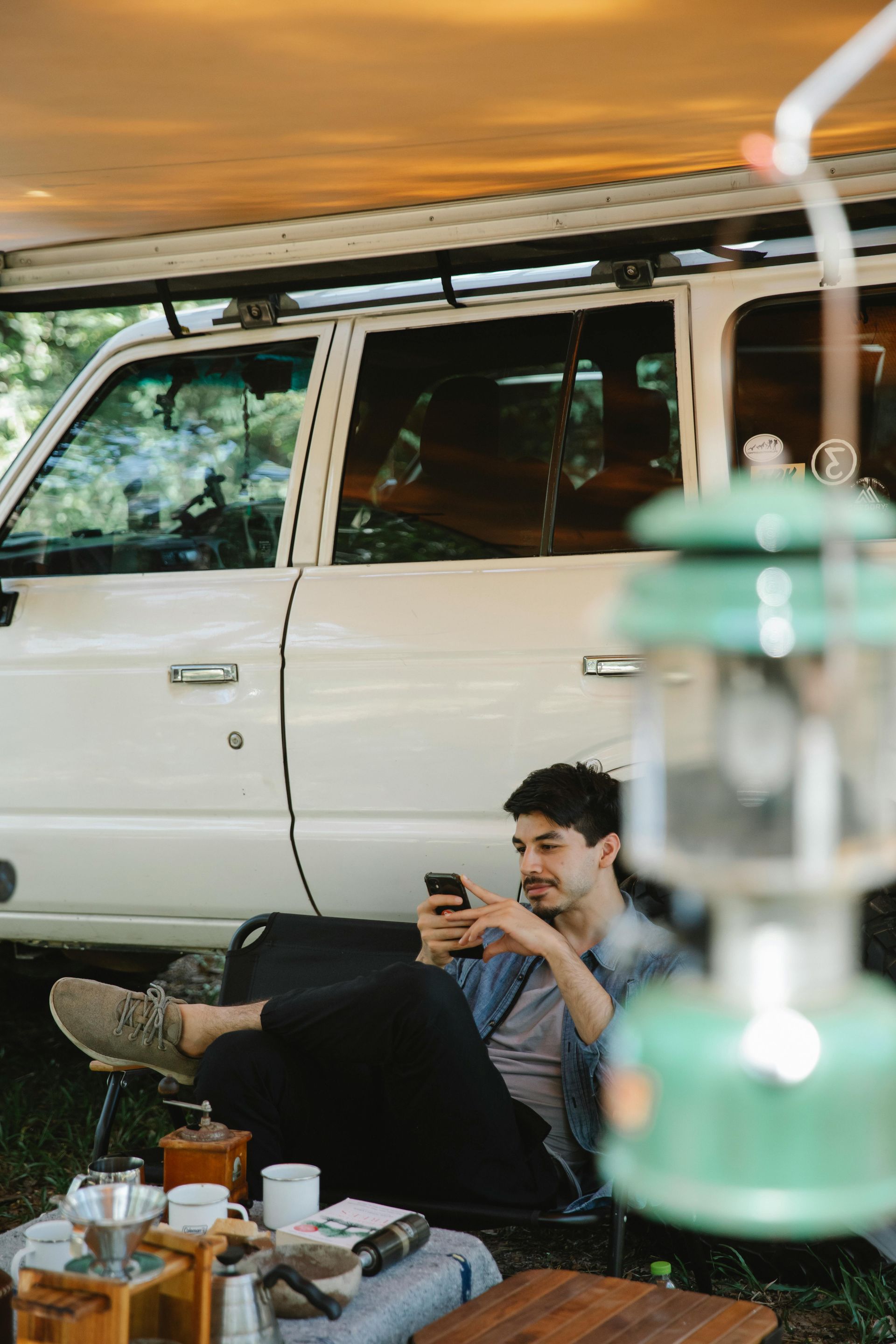 A man is sitting in front of a car looking at his phone.