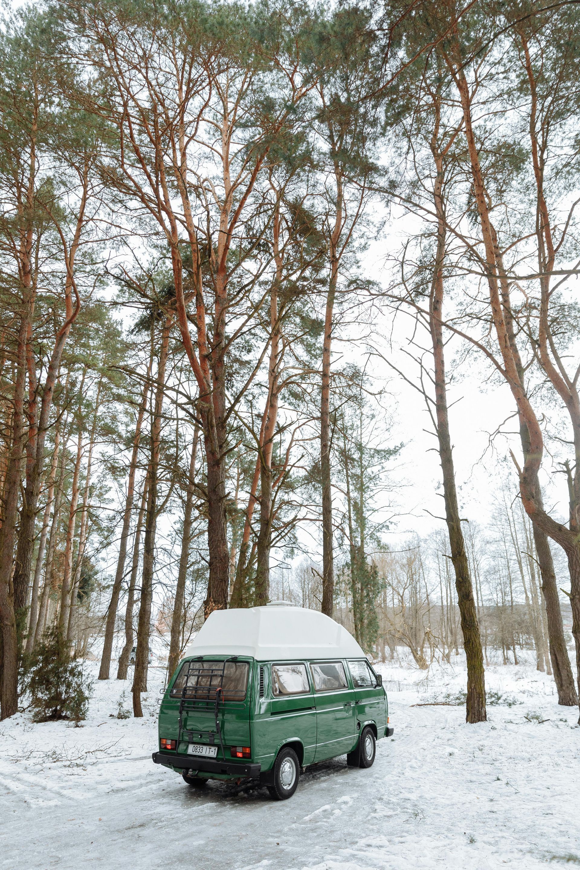 A green van is parked in the snow in a forest.