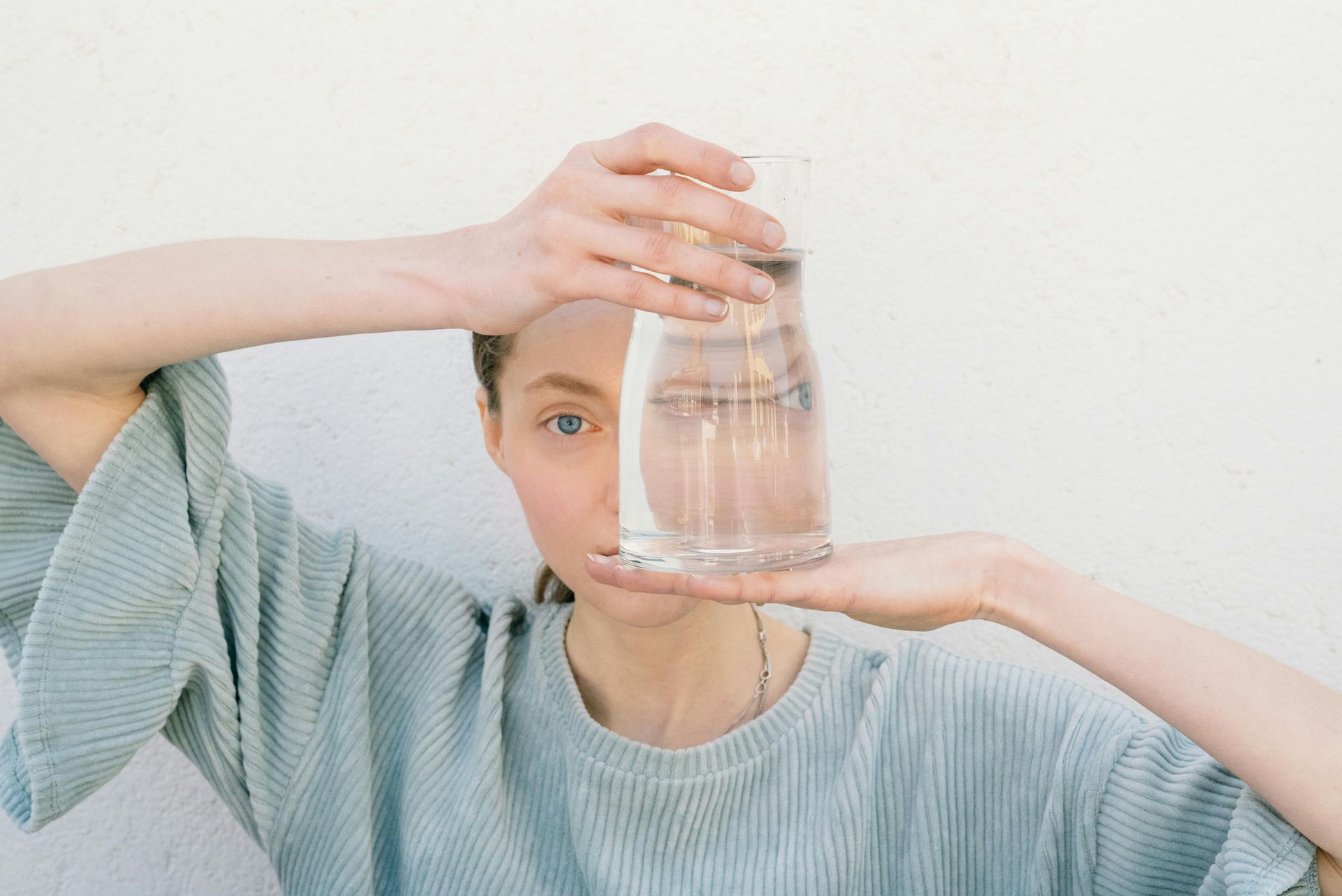 A woman is holding a glass of water in front of her face.