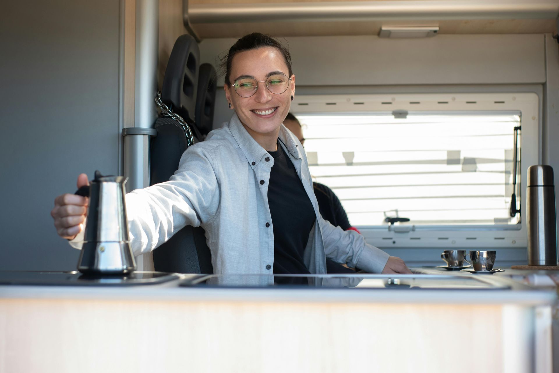 A man is standing in a camper van holding a coffee pot.