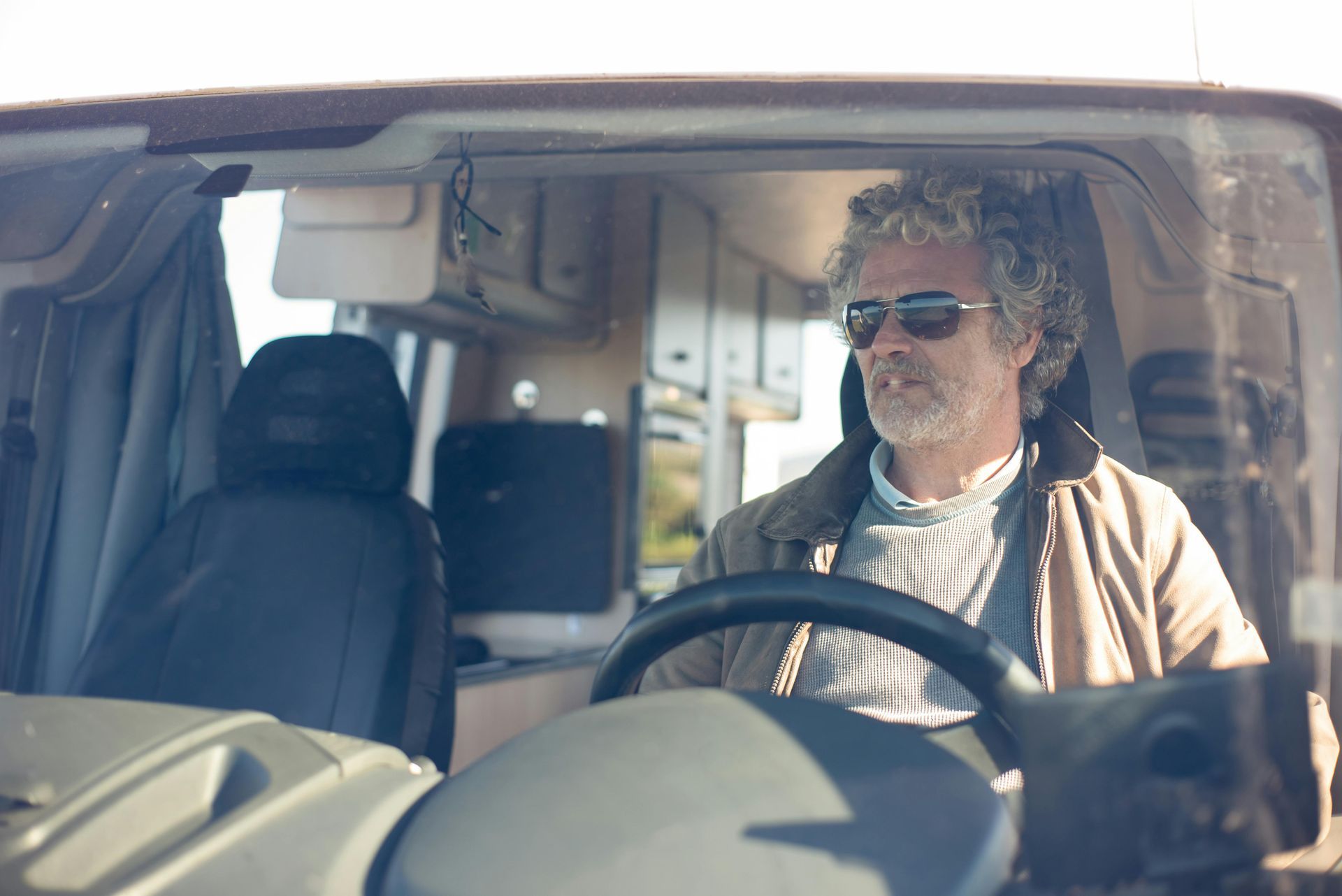 A man wearing sunglasses is driving a camper van.