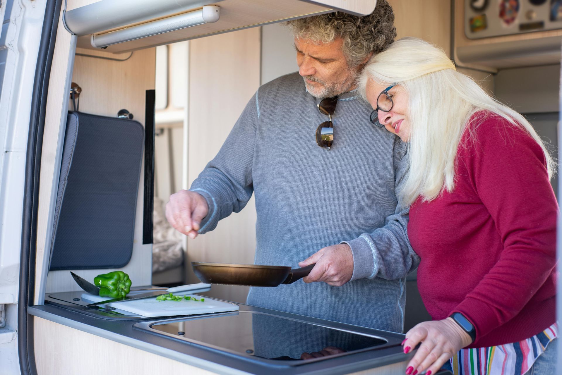 A man and a woman are cooking in a camper van.