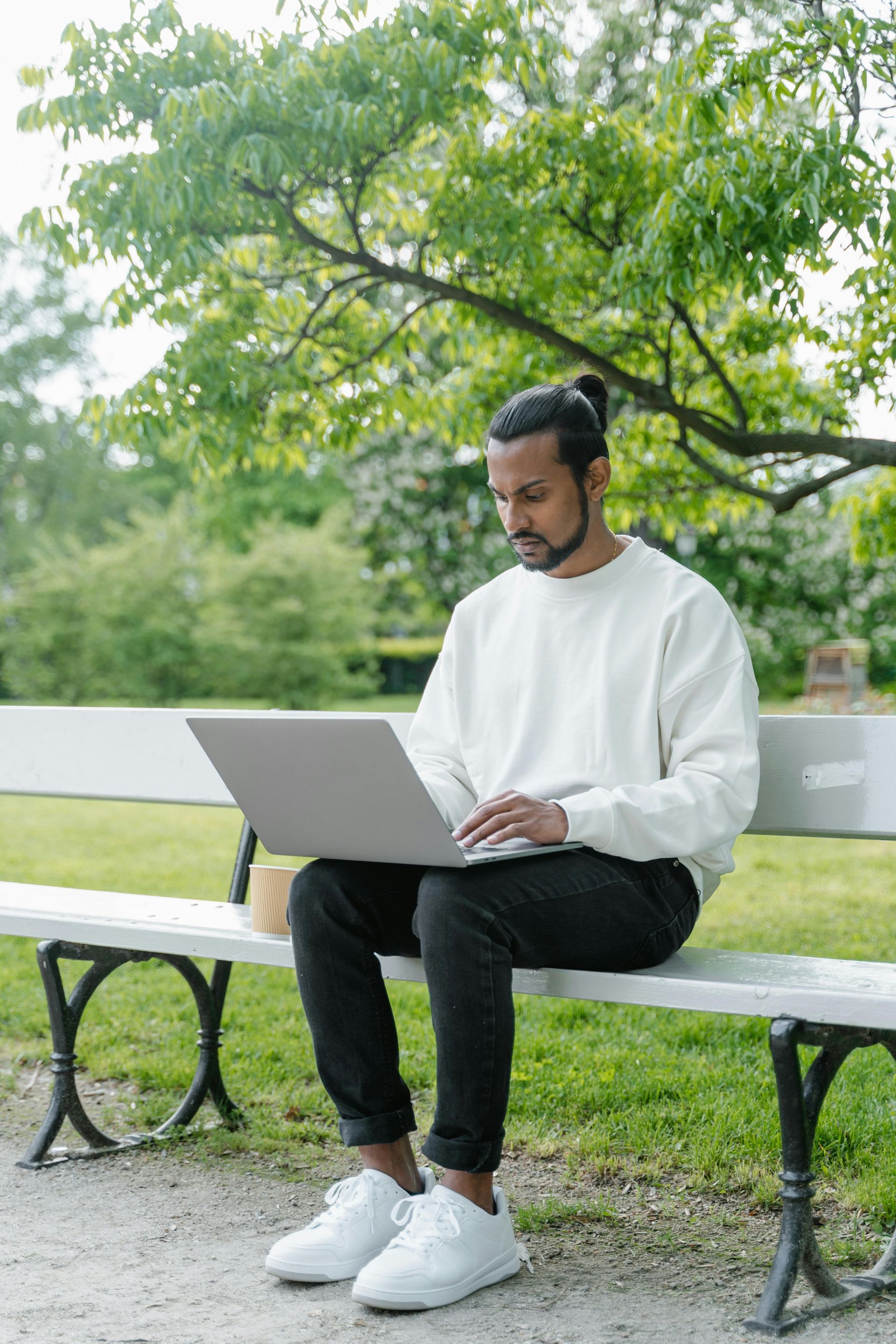 A man is sitting on a park bench using a laptop computer.