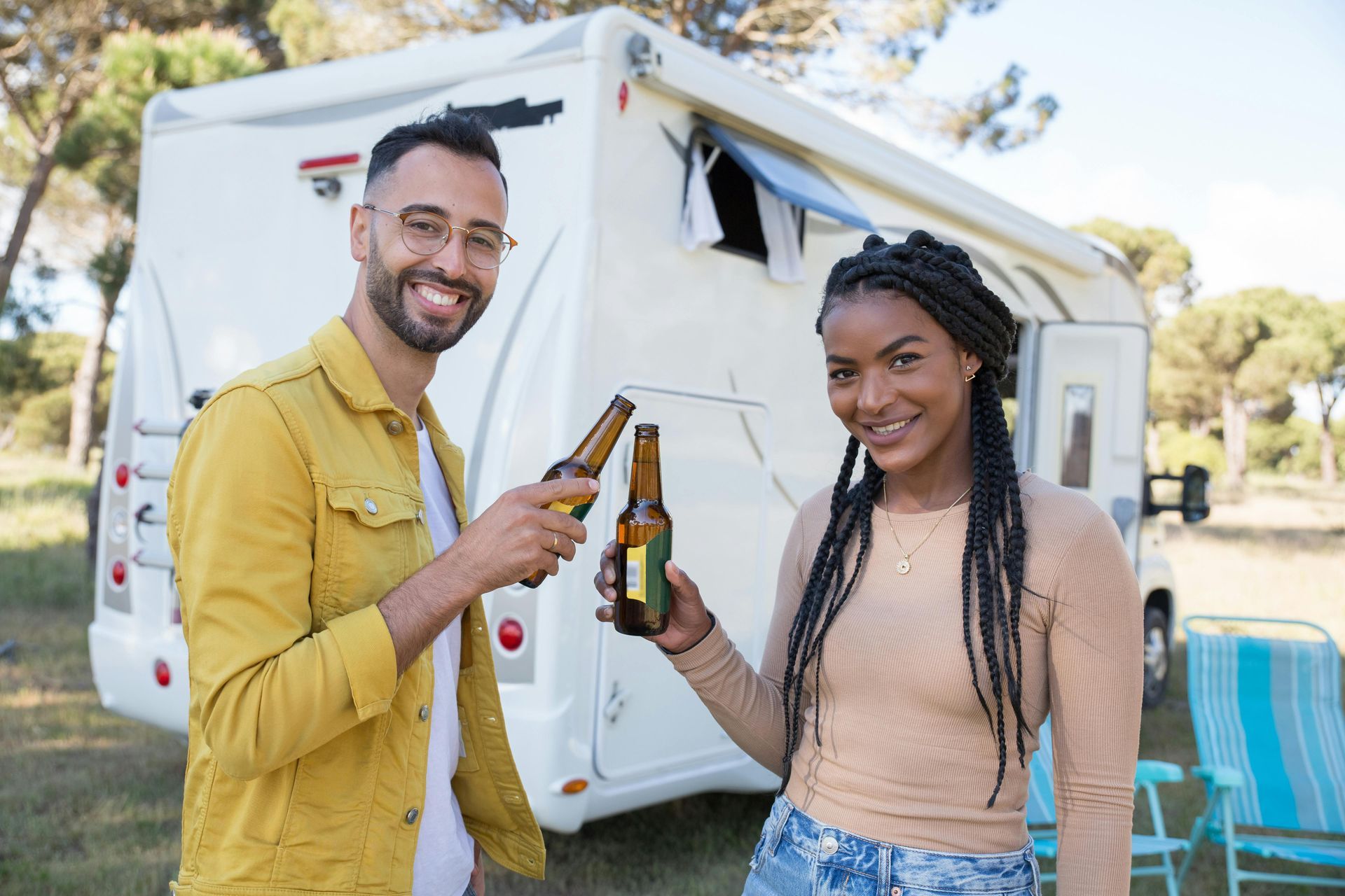 A man and a woman are toasting with beer in front of a camper van.